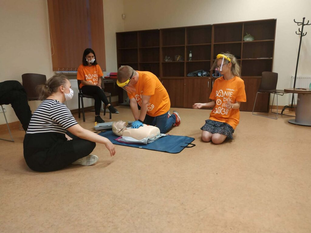 4 osoby siedzące na podłodze z fantomem podczas szkolenia z pierwszej pomocy